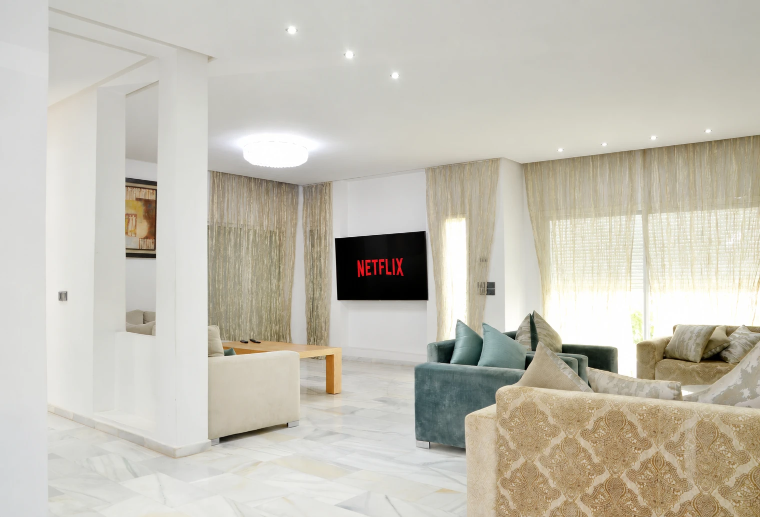 Salon lumineux aux canapés clairs et vert profond, avec Netflix sur le téléviseur